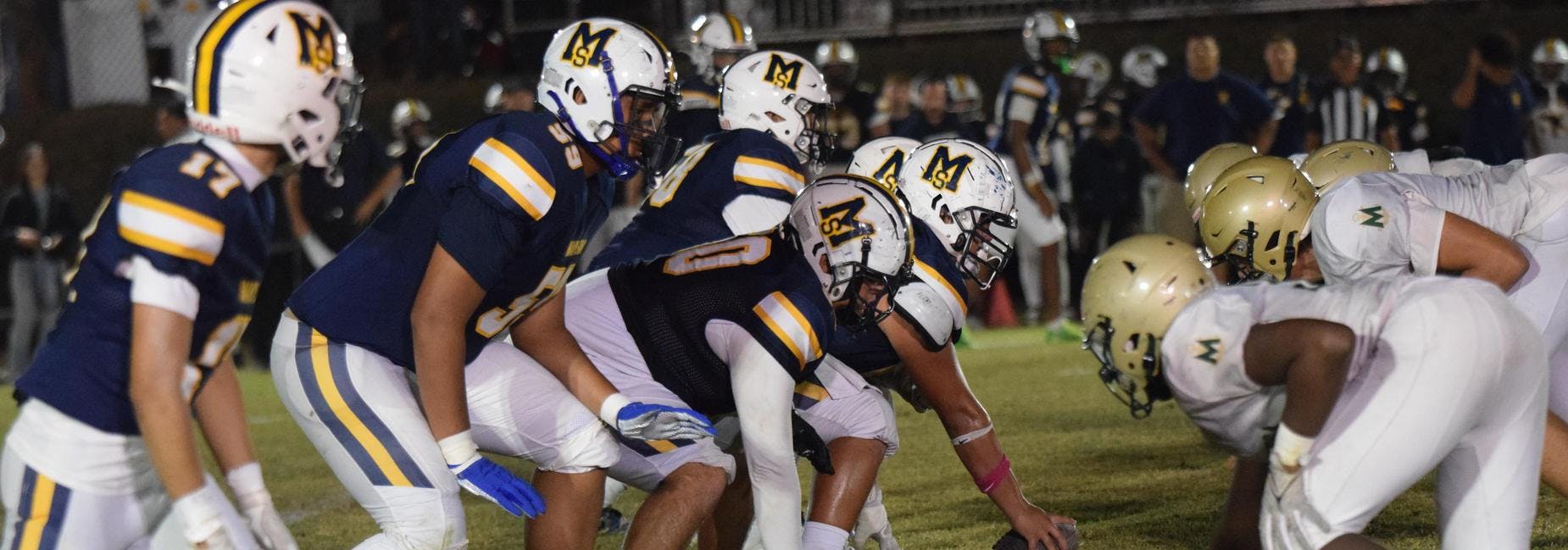 Football players in blue and gold uniforms facing off against players in white
