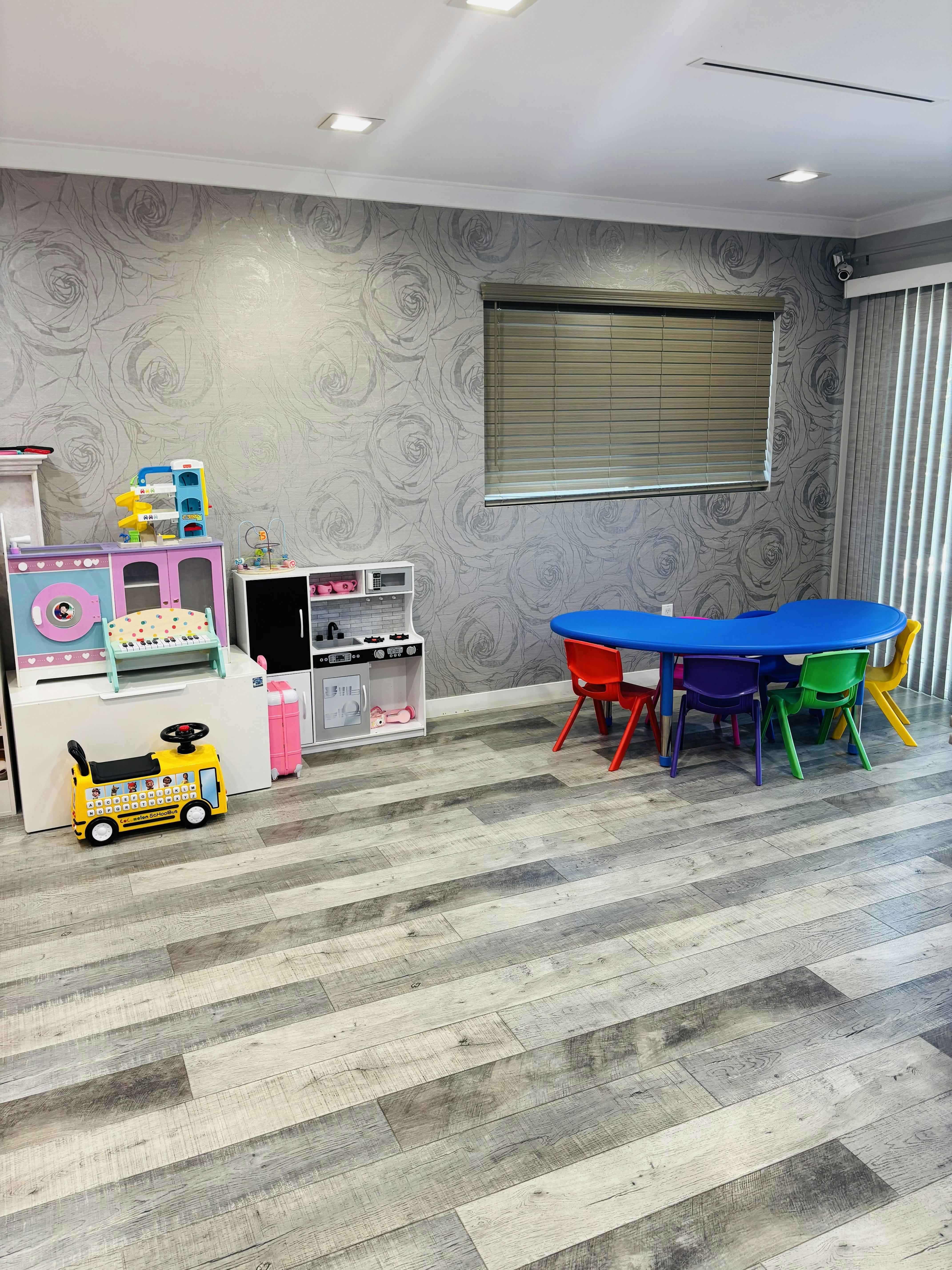 Children's play area with a blue table and colorful chairs, toy kitchen, and ride-on school bus