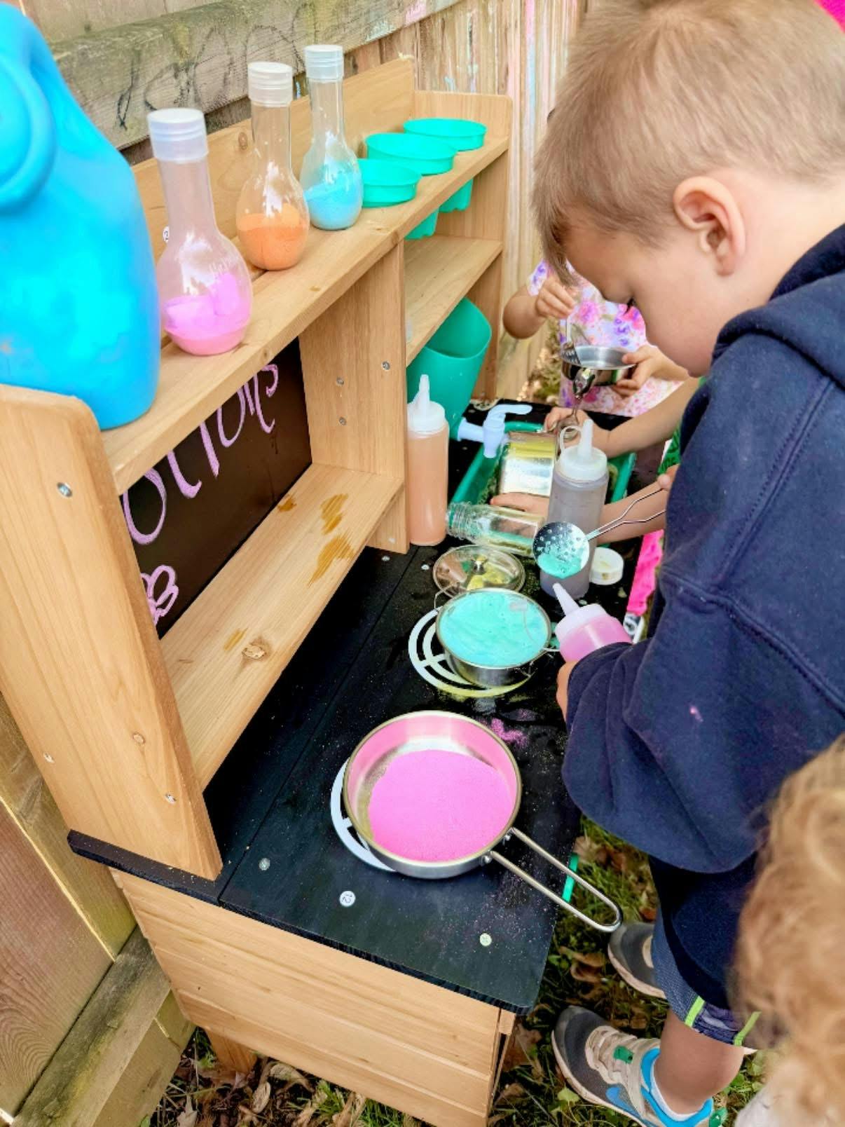 Children playing with colorful sand at a wooden toy kitchen station