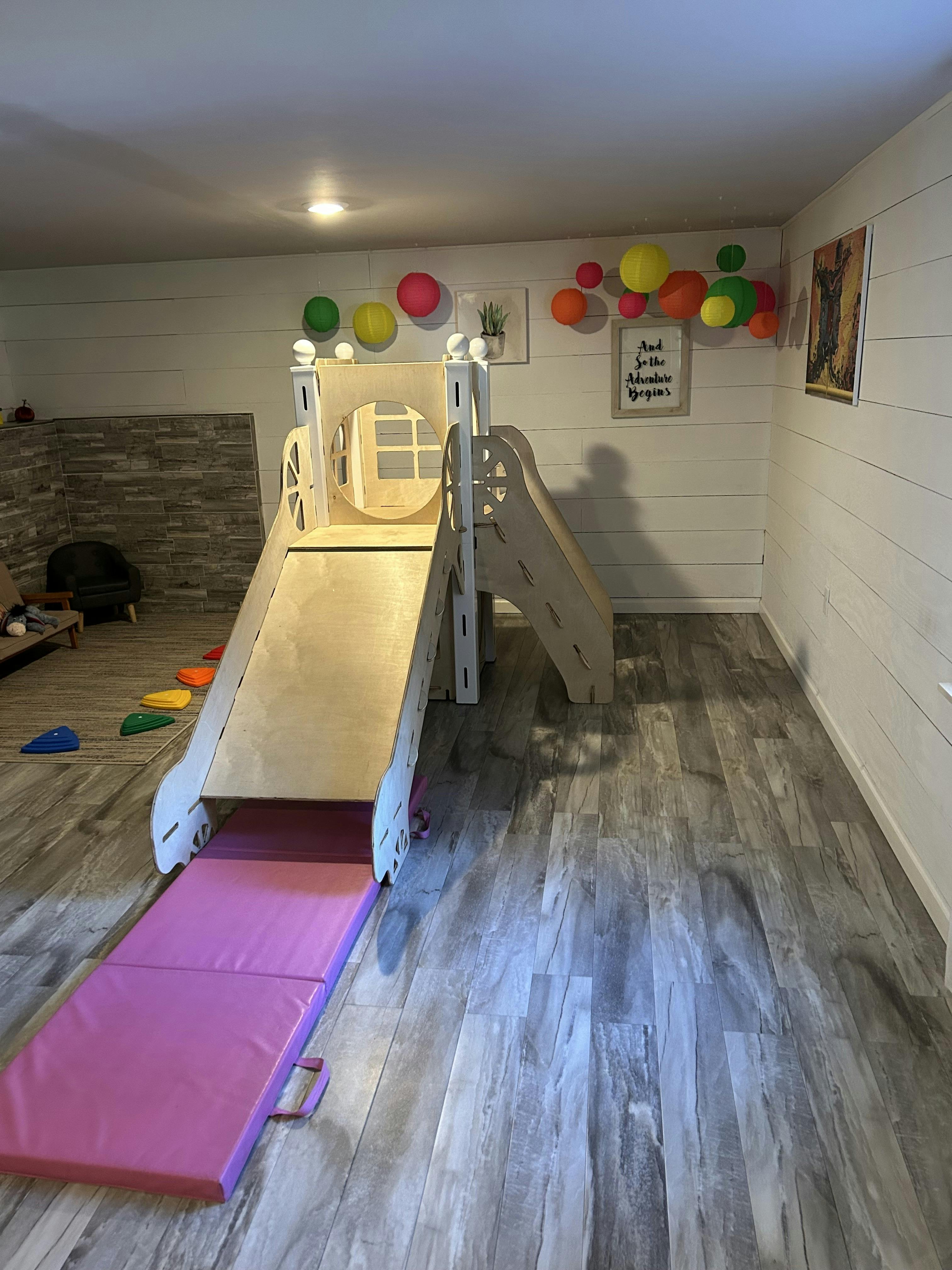 Indoor wooden play structure with a slide and a purple mat