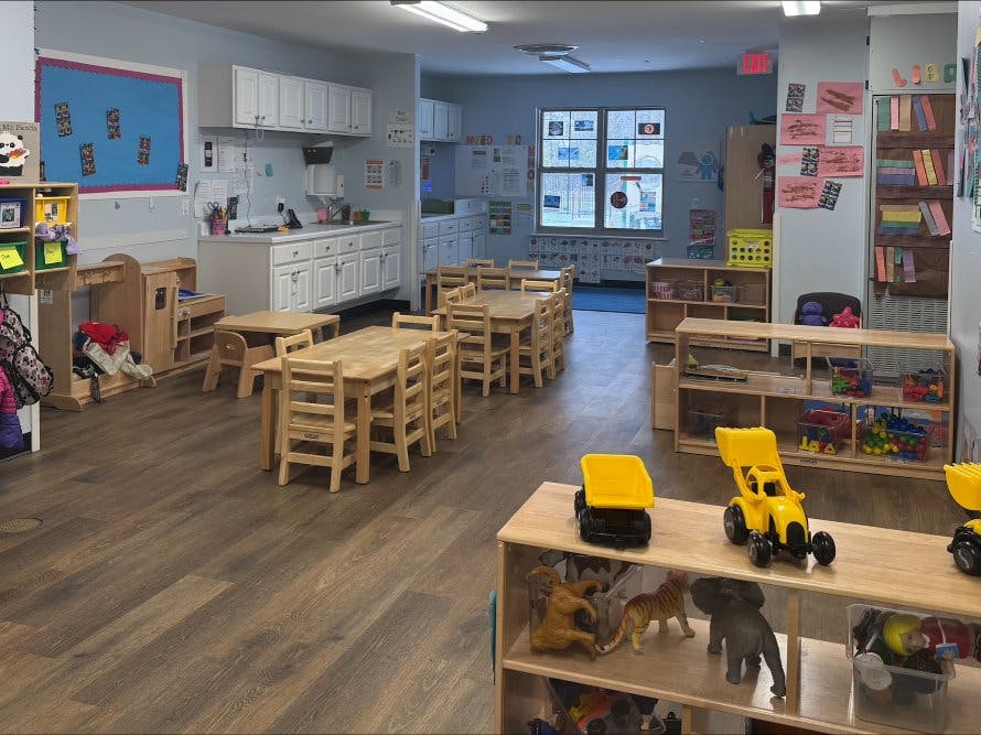 Children's classroom with small tables and chairs, a kitchen area, and toy shelves