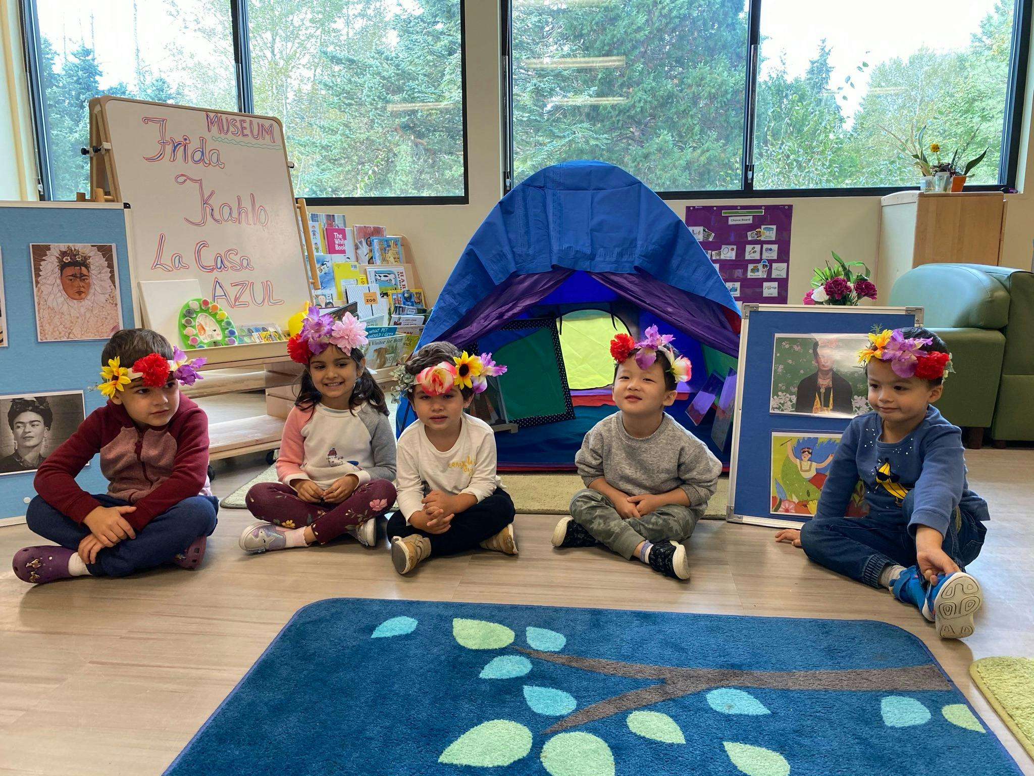 Five children wearing flower headbands sitting on the floor in a classroom