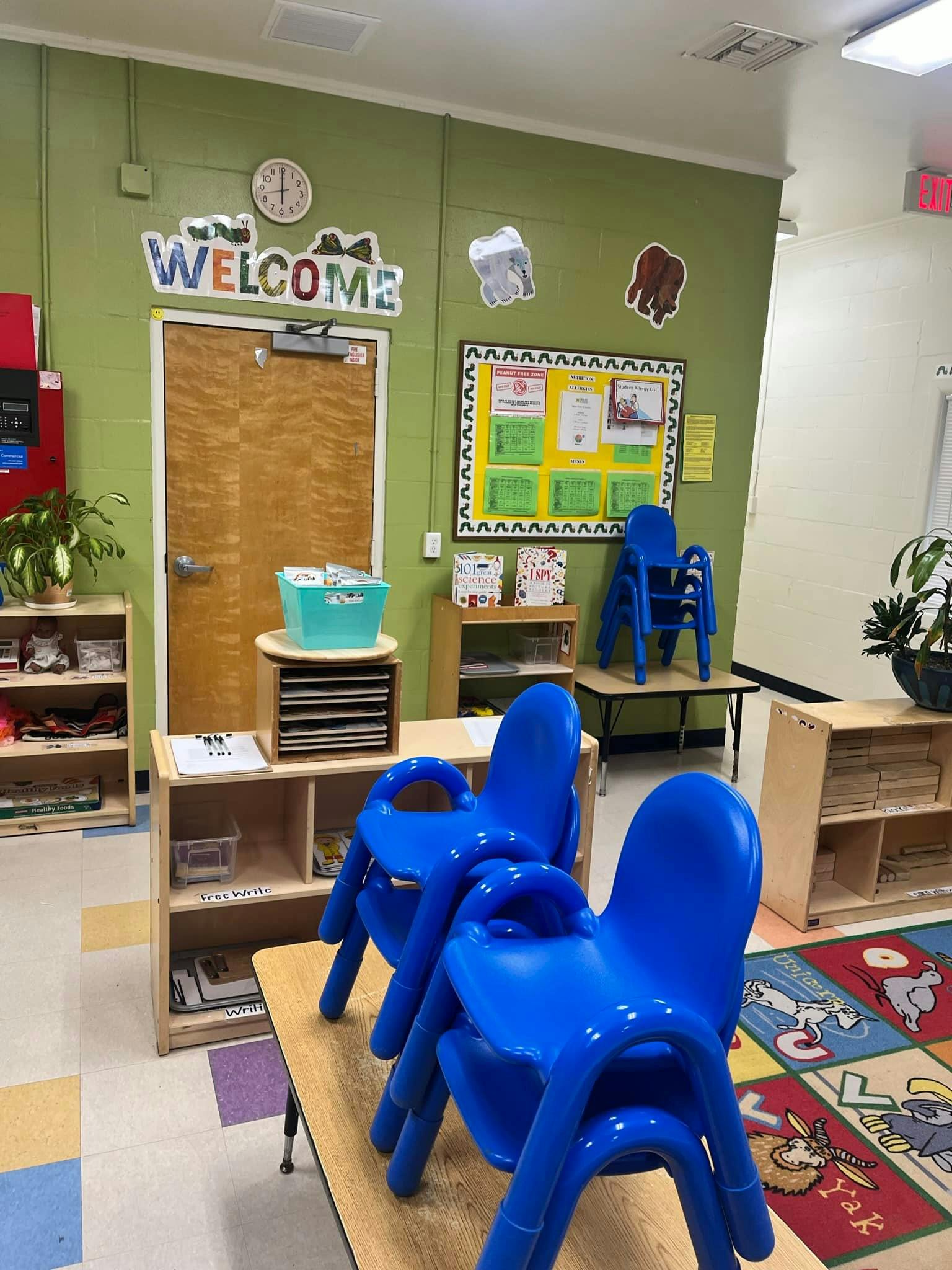 Classroom with child-sized blue chairs, tables, and a WELCOME sign above a door