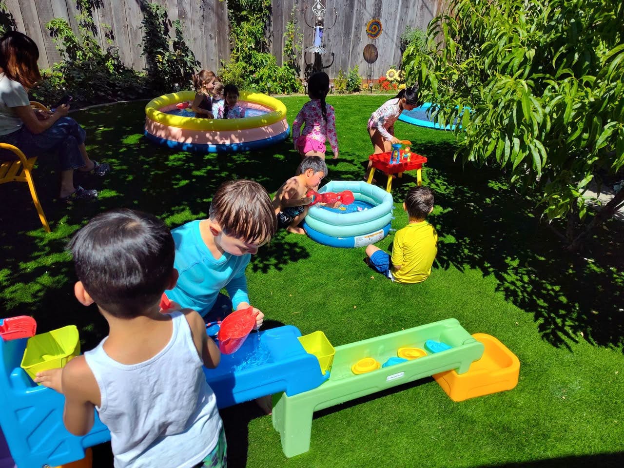 Children playing with water toys and inflatable pools on grass in a backyard