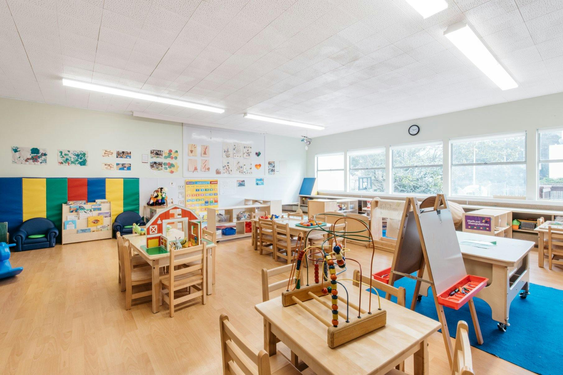 Empty preschool classroom with wooden tables and chairs, toys, and colorful decorations