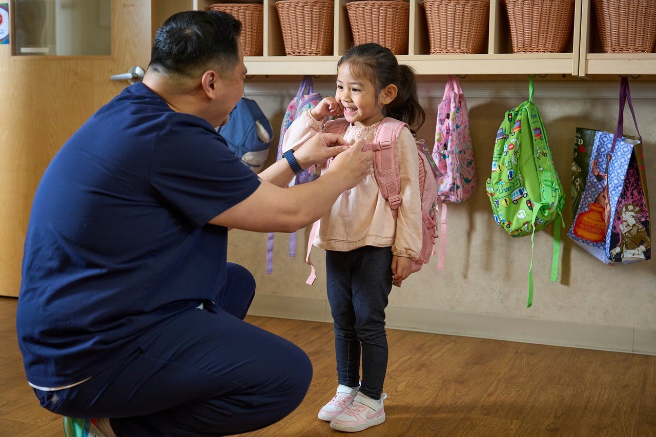 Person helping a child put on a backpack