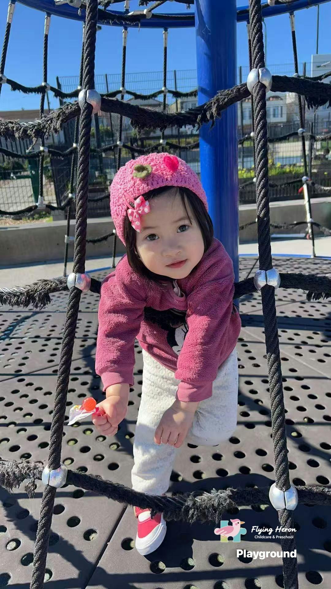 Child in a pink hat on a rope climbing structure