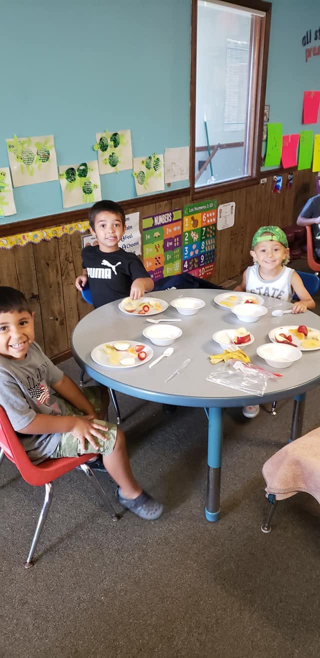 Three children sitting at a table with plates of food