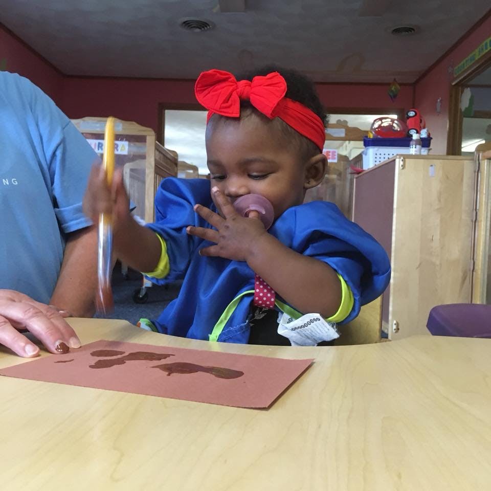 Child with pacifier painting on paper at a table