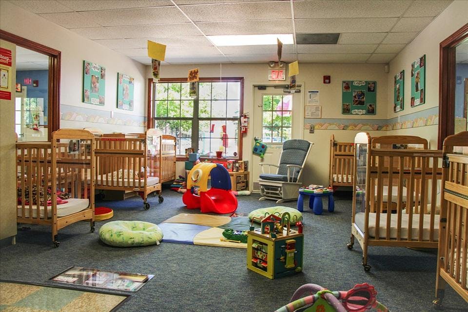 A room with several cribs, a red slide, and a rocking chair