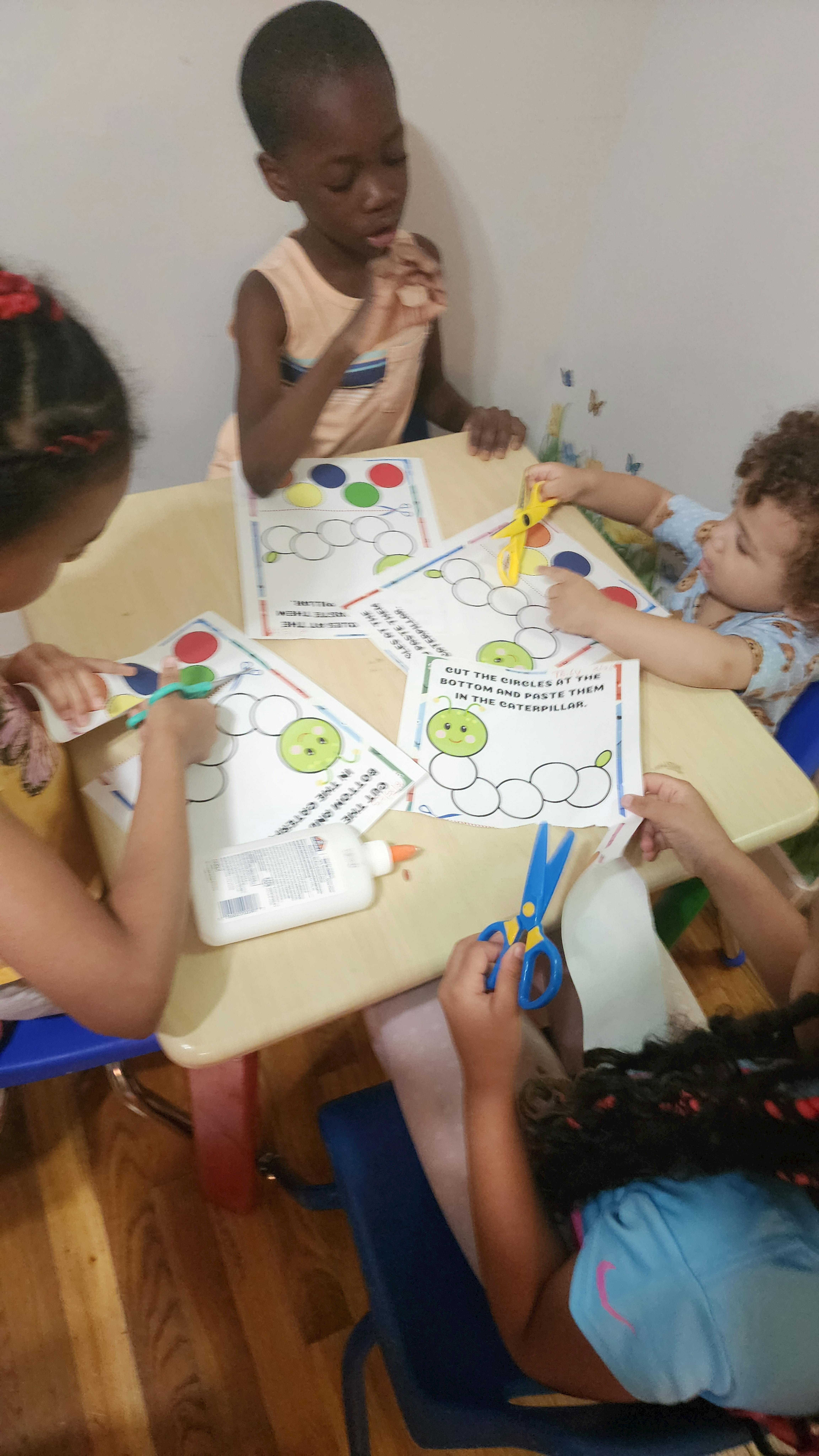Children at a table doing a craft with paper, scissors, and glue