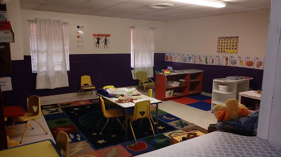 Classroom with small tables and chairs, colorful rug, and wall decorations