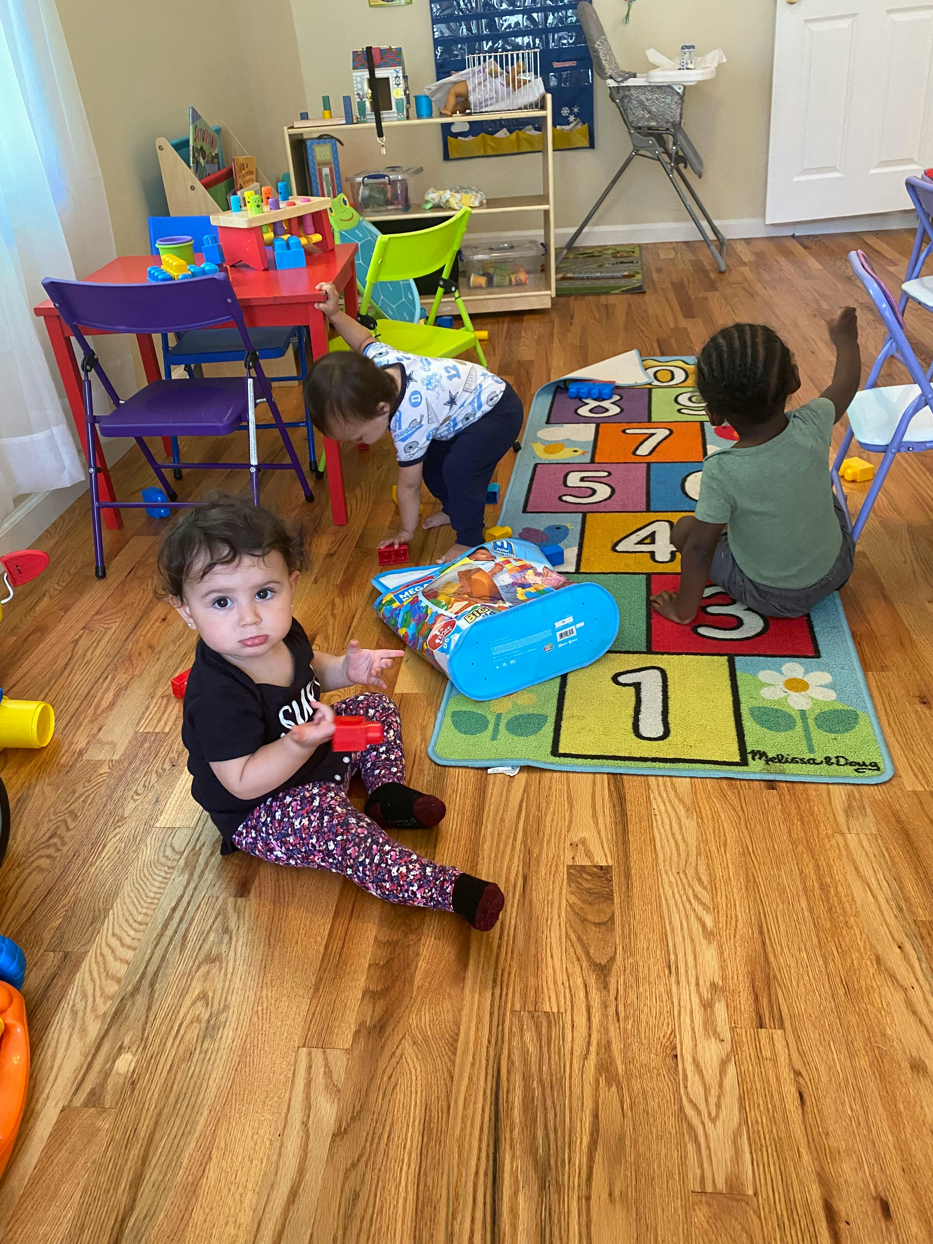Three children playing on a wooden floor with a number mat