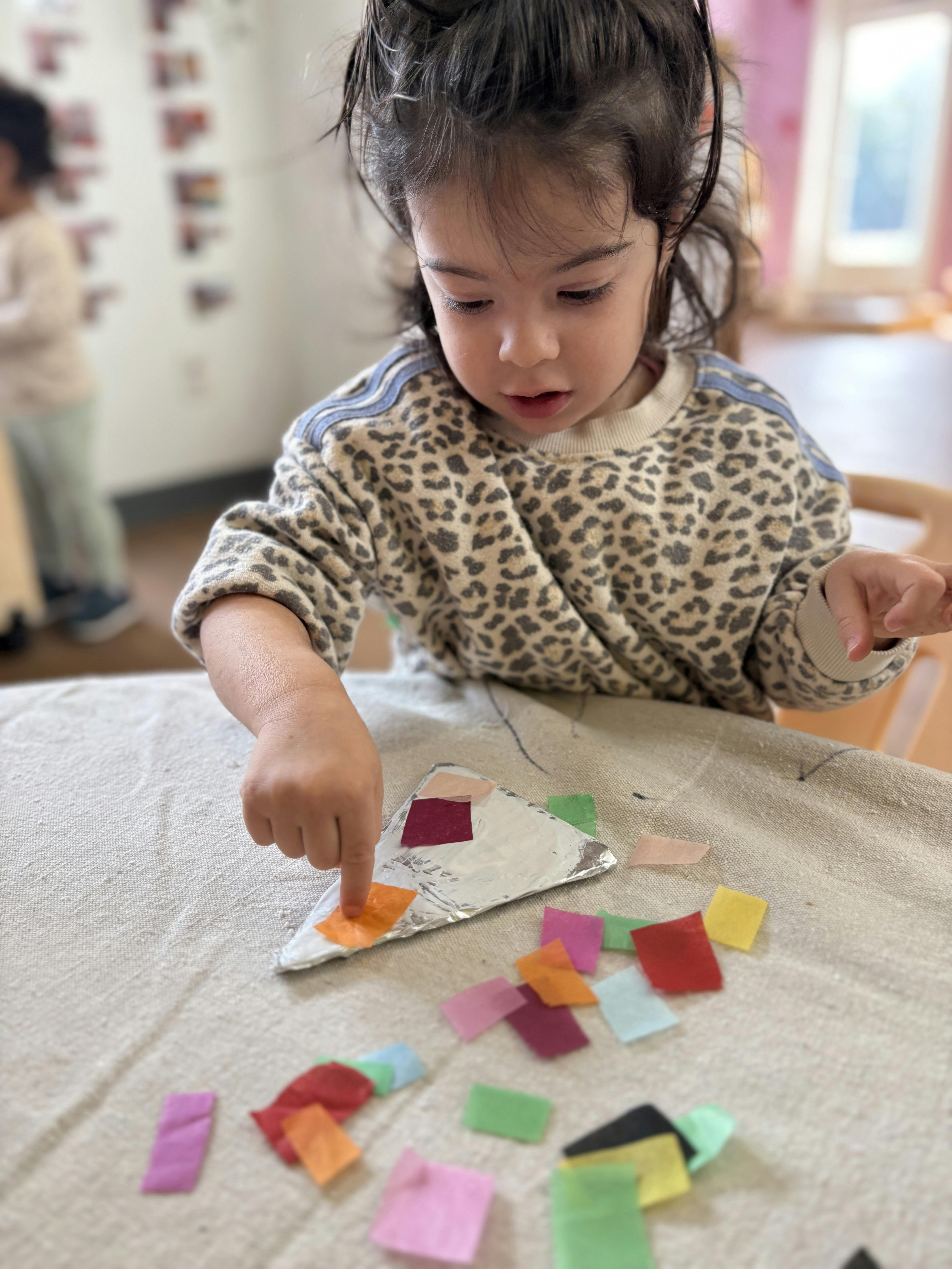 Child placing colorful paper squares on a foil-covered triangle shape
