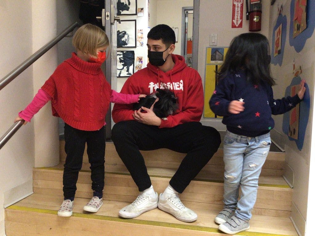 Person in mask holding small animal with two children