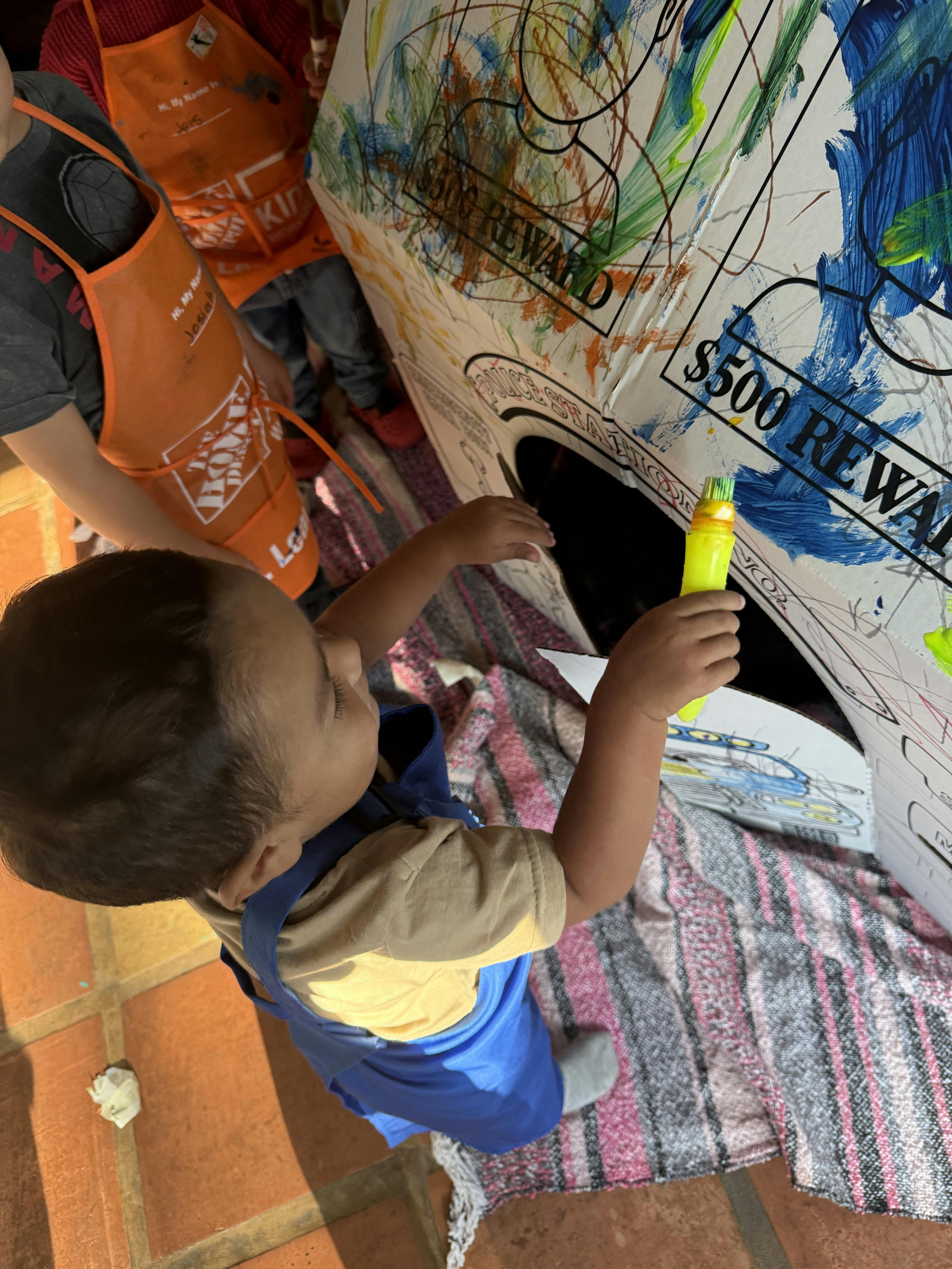Child painting a large box with a paint stick