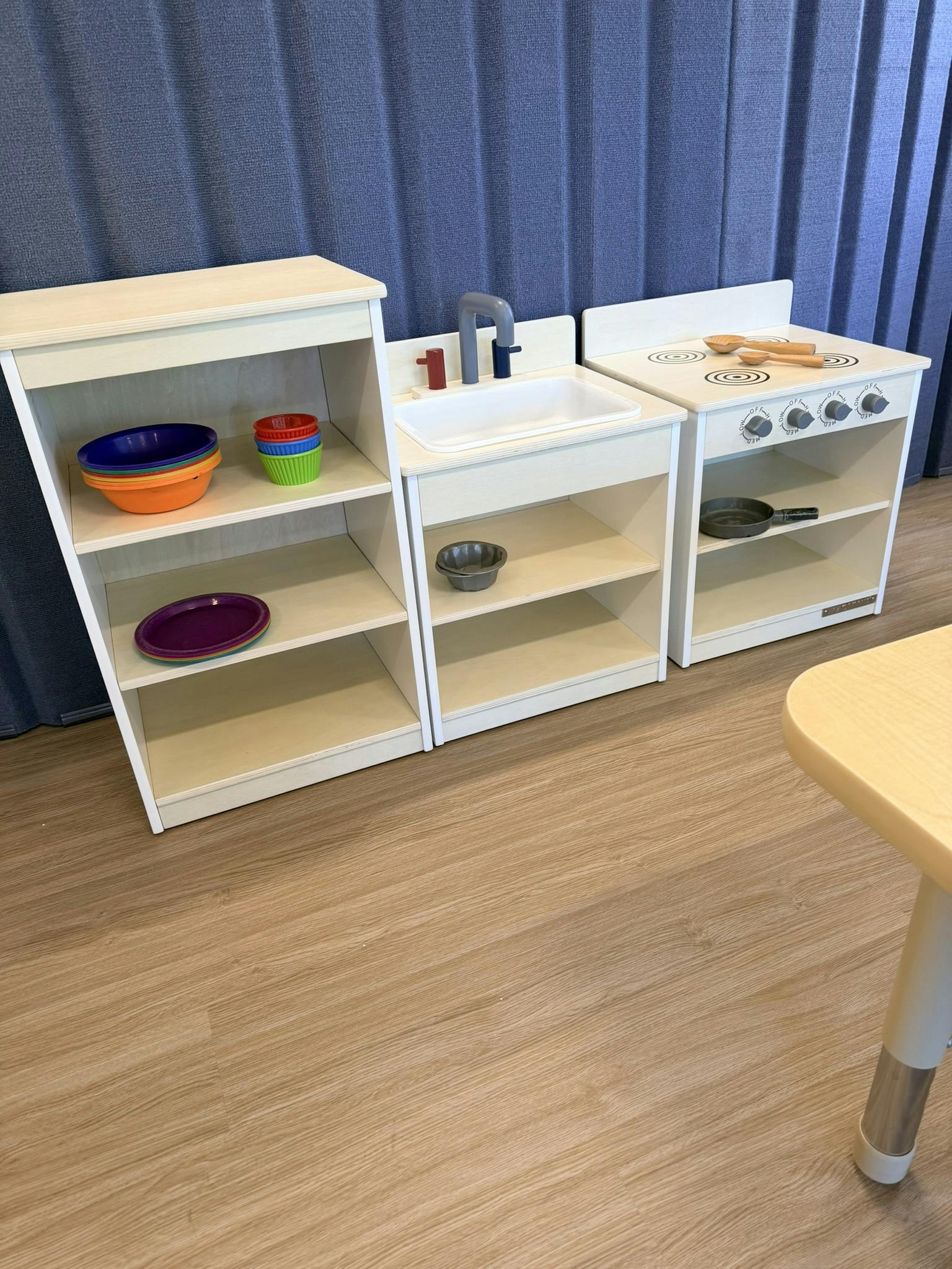 A wooden play kitchen set with colorful bowls and plates