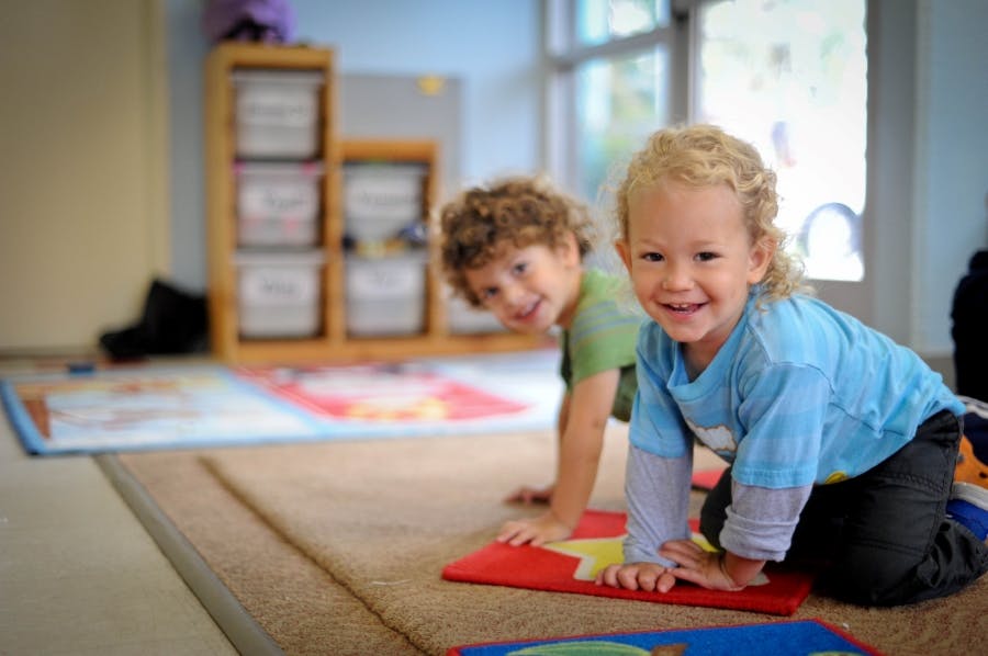 Two children on hands and knees on mats in a classroom