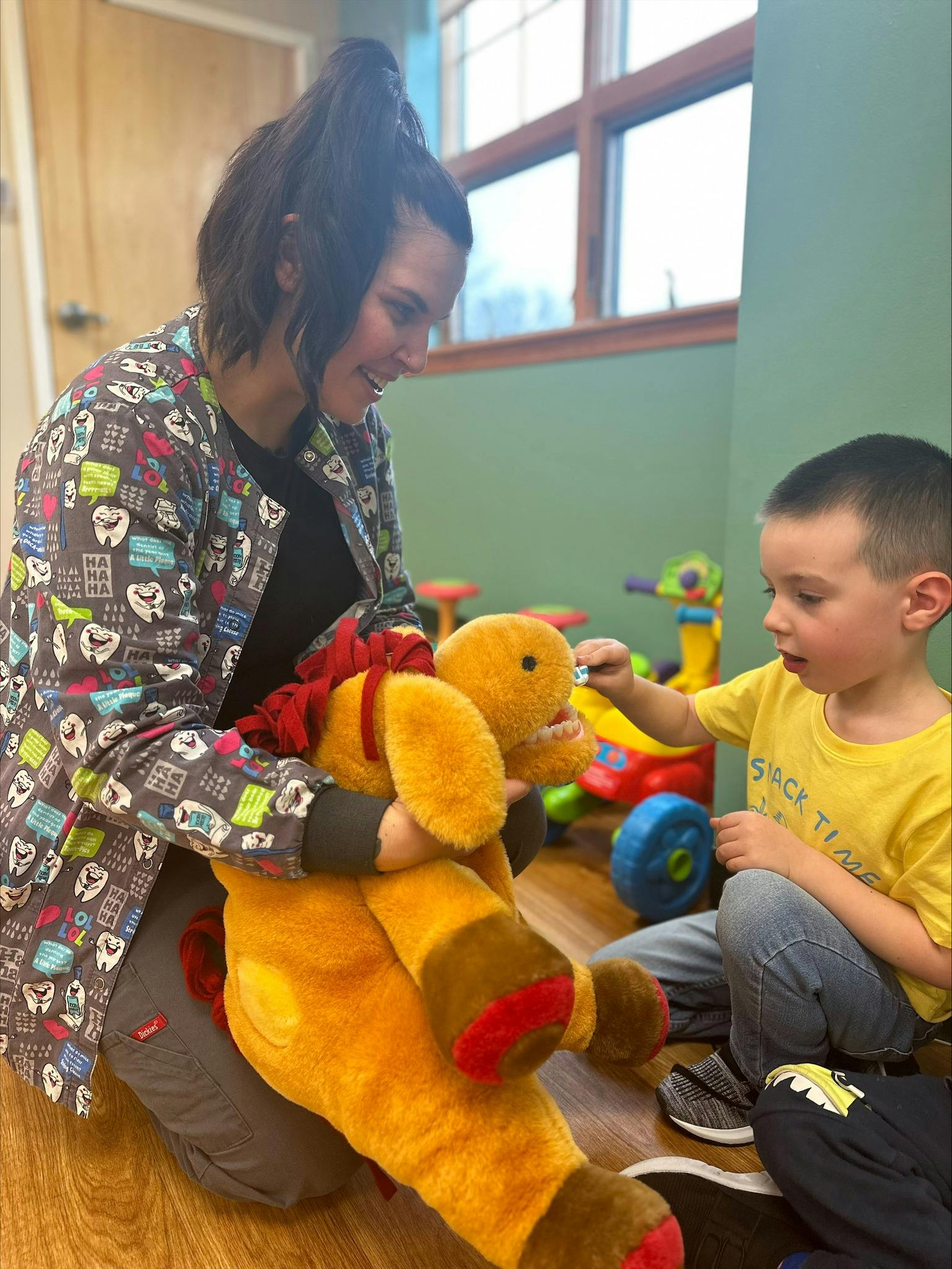 Person in scrubs holding a stuffed animal while a child plays with it