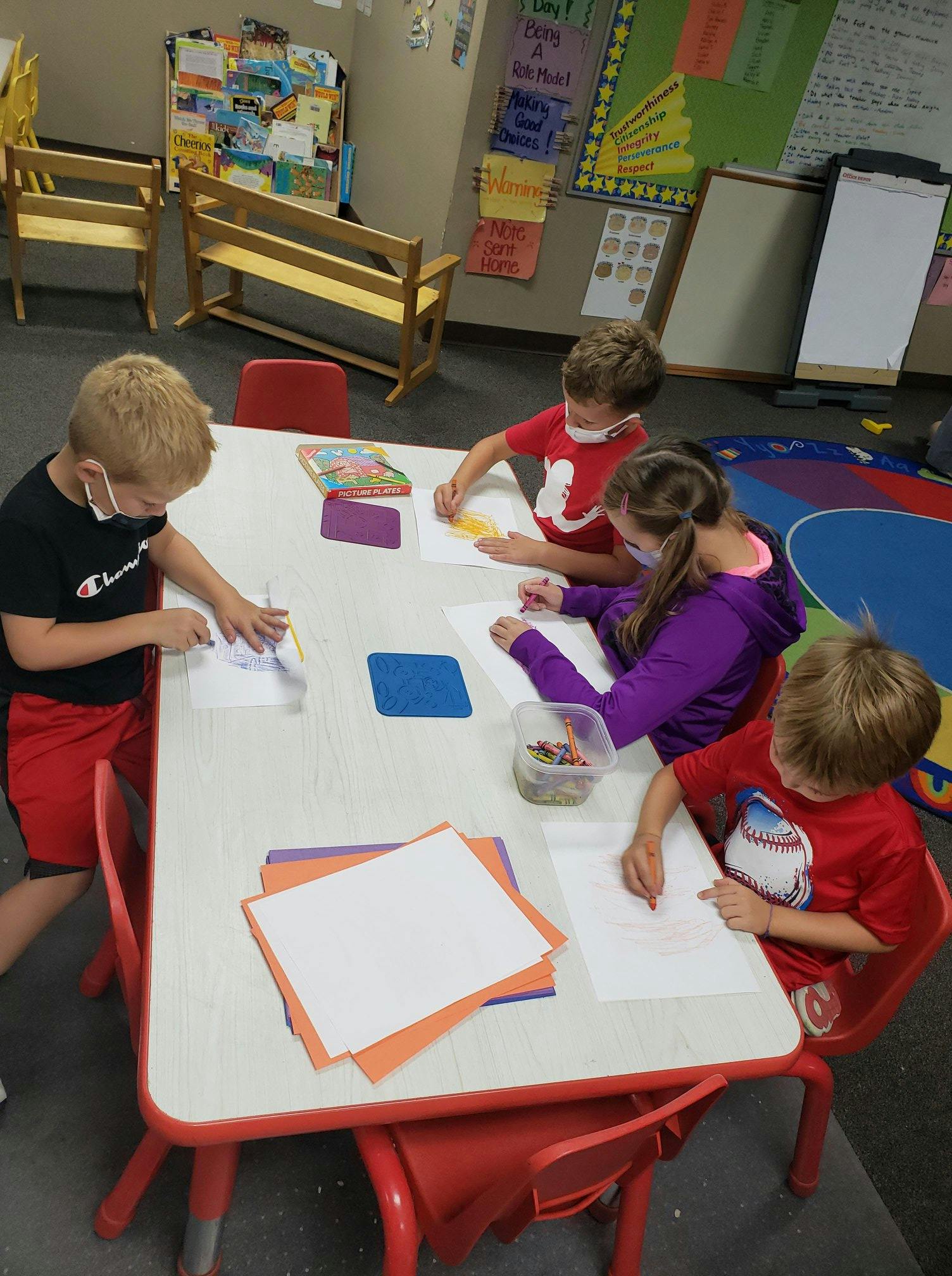 Four children drawing at a table in a classroom
