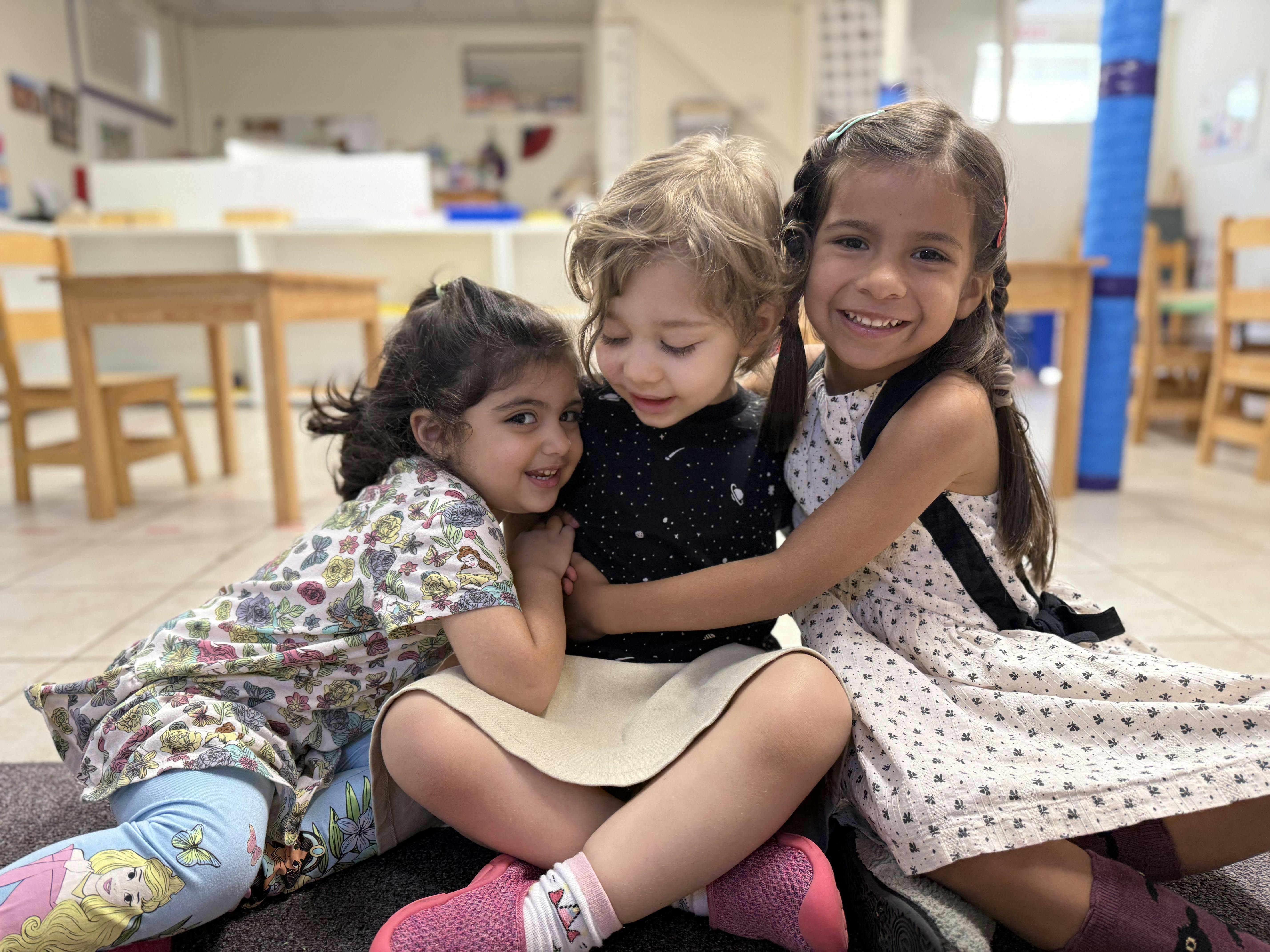 Three children hugging each other while sitting in a classroom