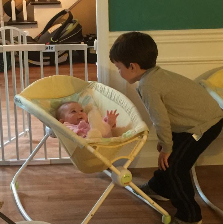 Child looking at a baby in a bouncer