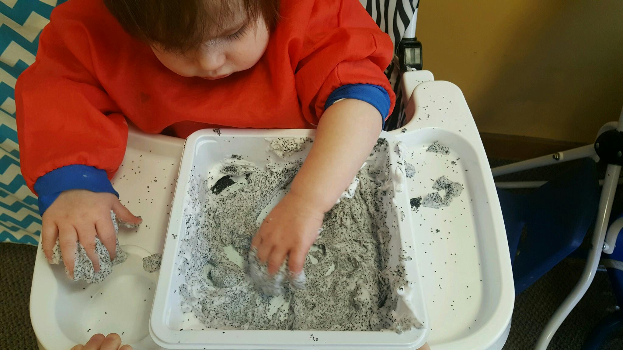 Child in high chair playing with sensory bin