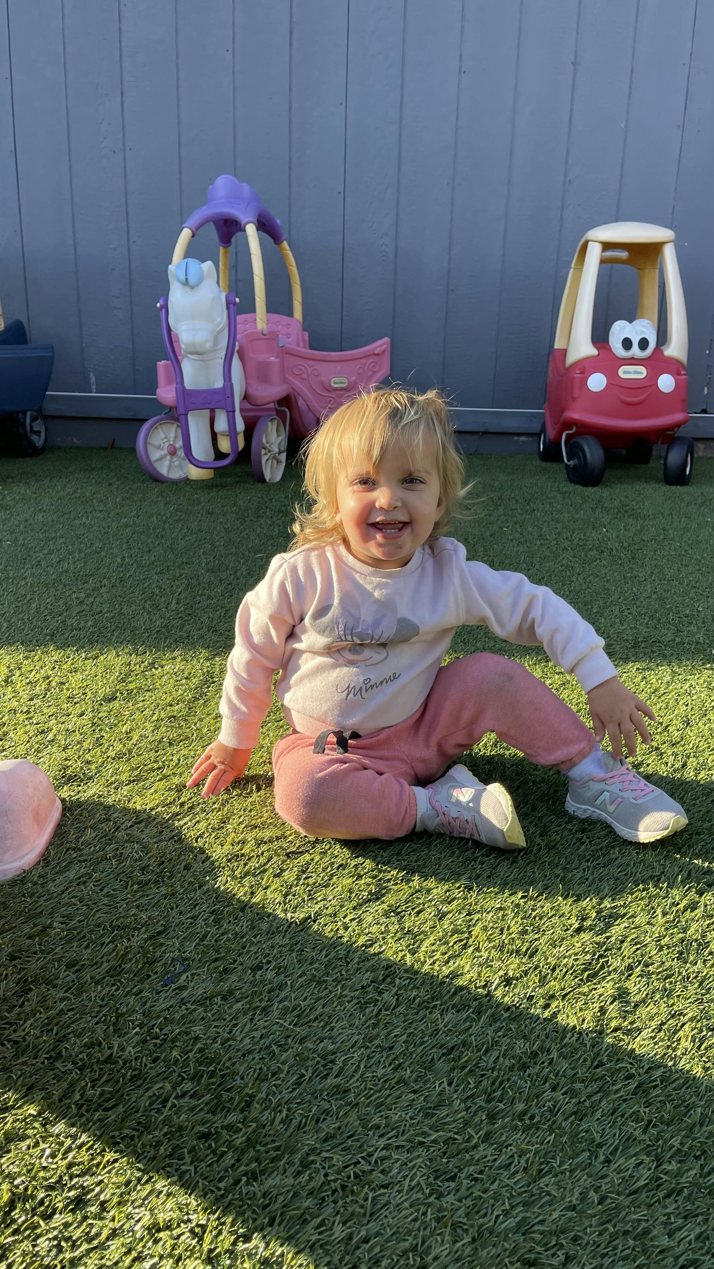 Child sitting on green artificial grass, smiling at the camera