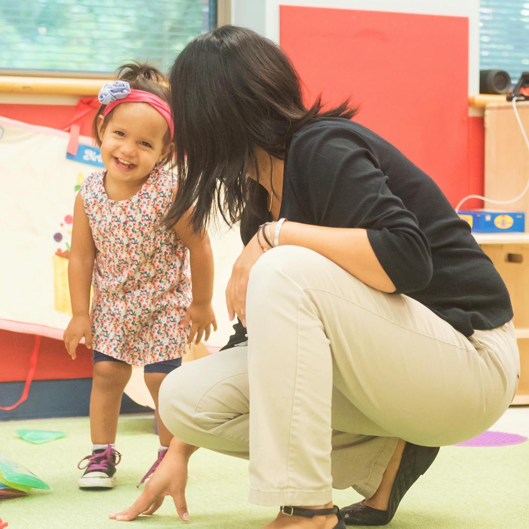 Adult crouching and looking at a child in a classroom