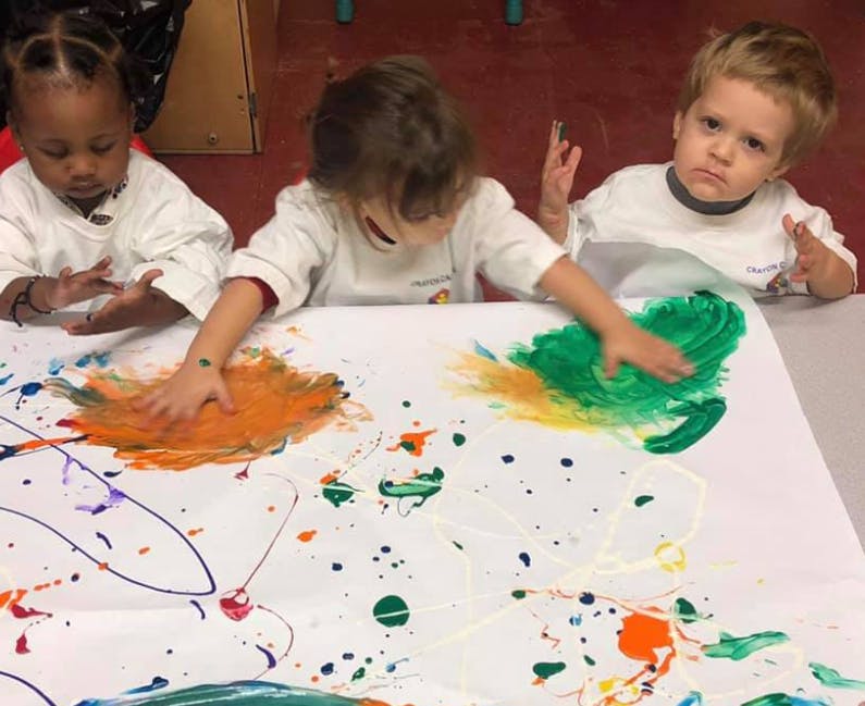 Three children finger painting on a large white sheet