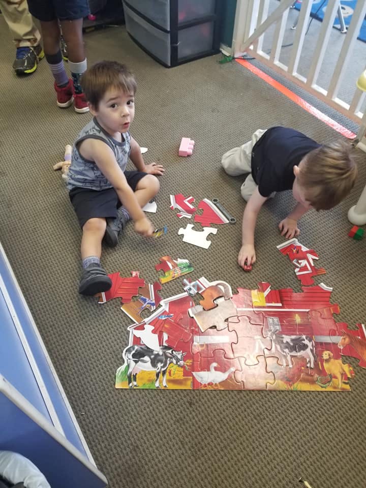 Two children playing with a farm animal puzzle on the floor