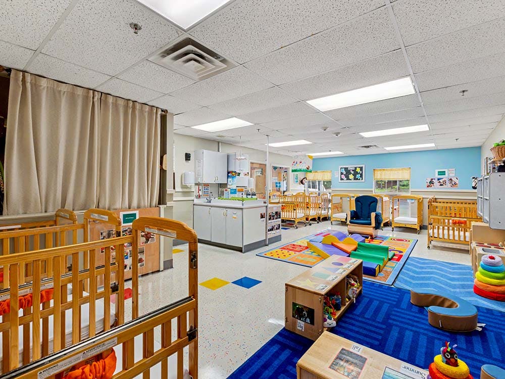 A childcare classroom with multiple wooden cribs, playmats, and cabinets