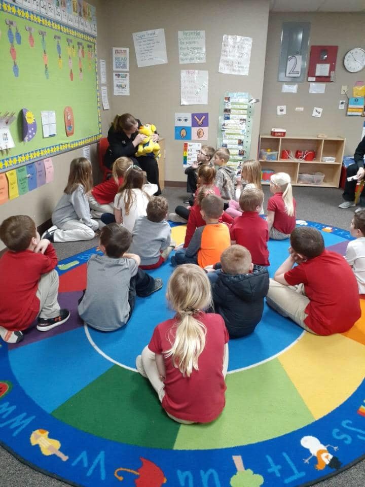 Adult reading to children sitting on a colorful rug in a classroom