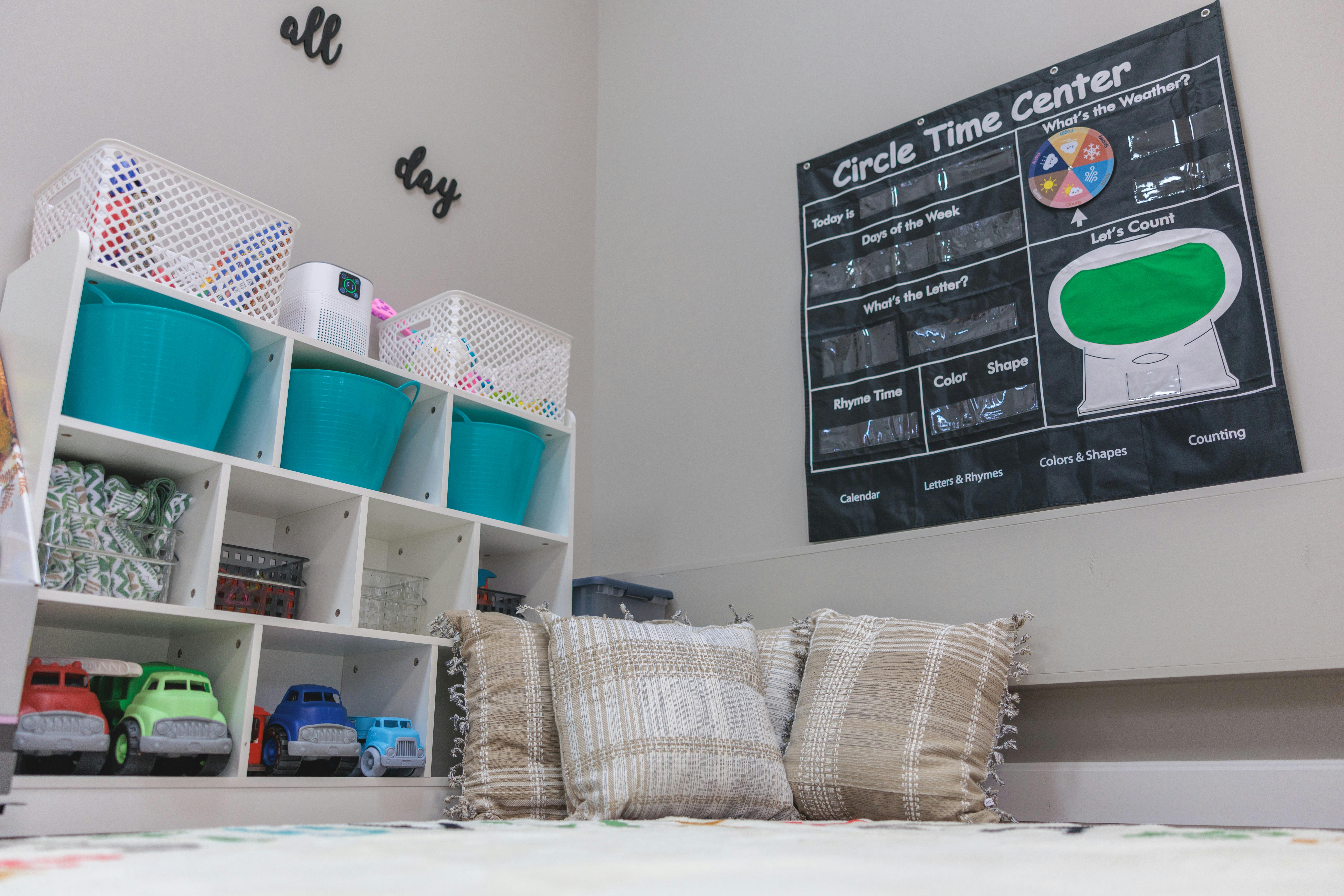 Storage shelves with toys and bins next to a wall chart and pillows