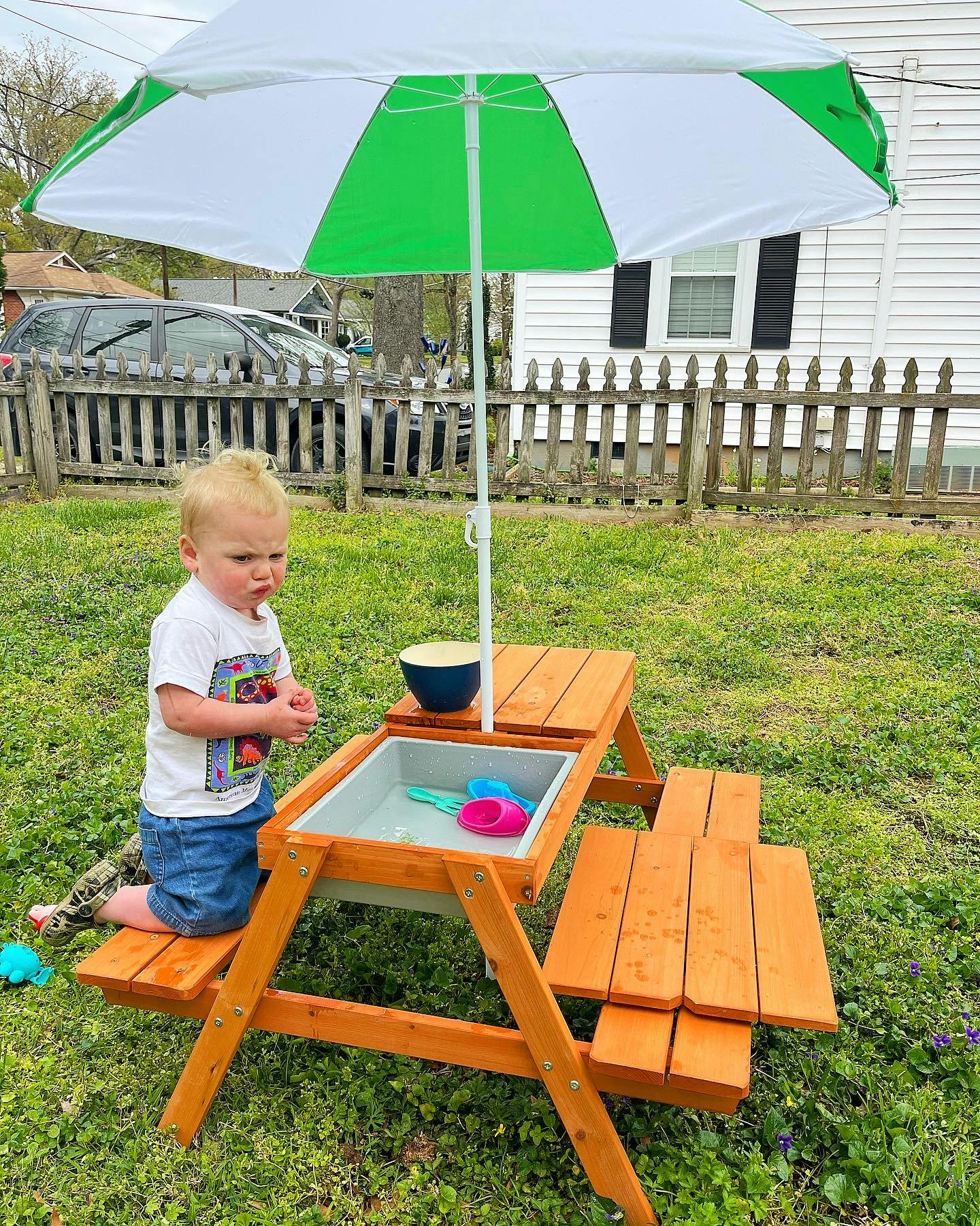 Child kneeling at a wooden play table with a water basin under an umbrella