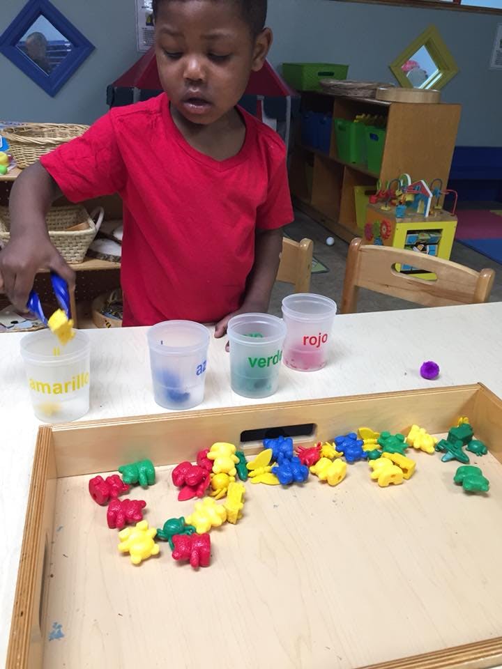 Child using tongs to pick up a yellow toy from a tray