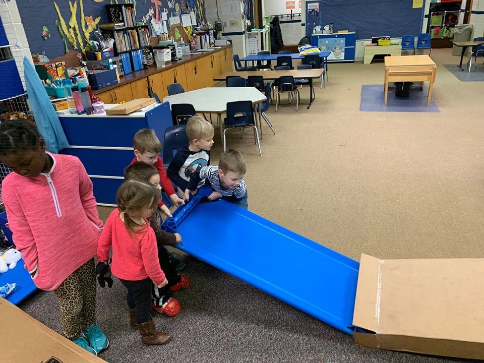 Children playing with a blue slide in a classroom