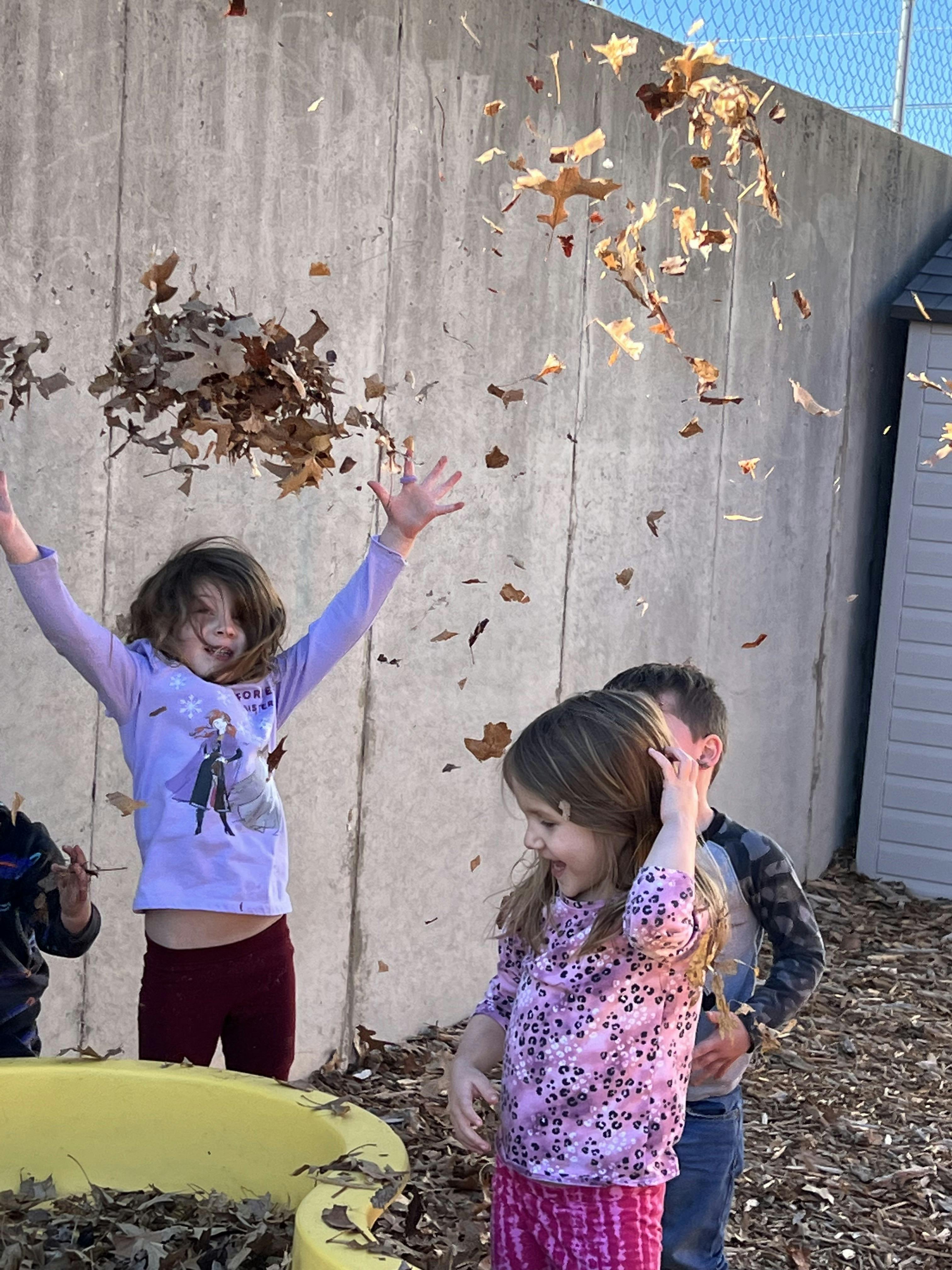Children throwing dry leaves into the air outdoors
