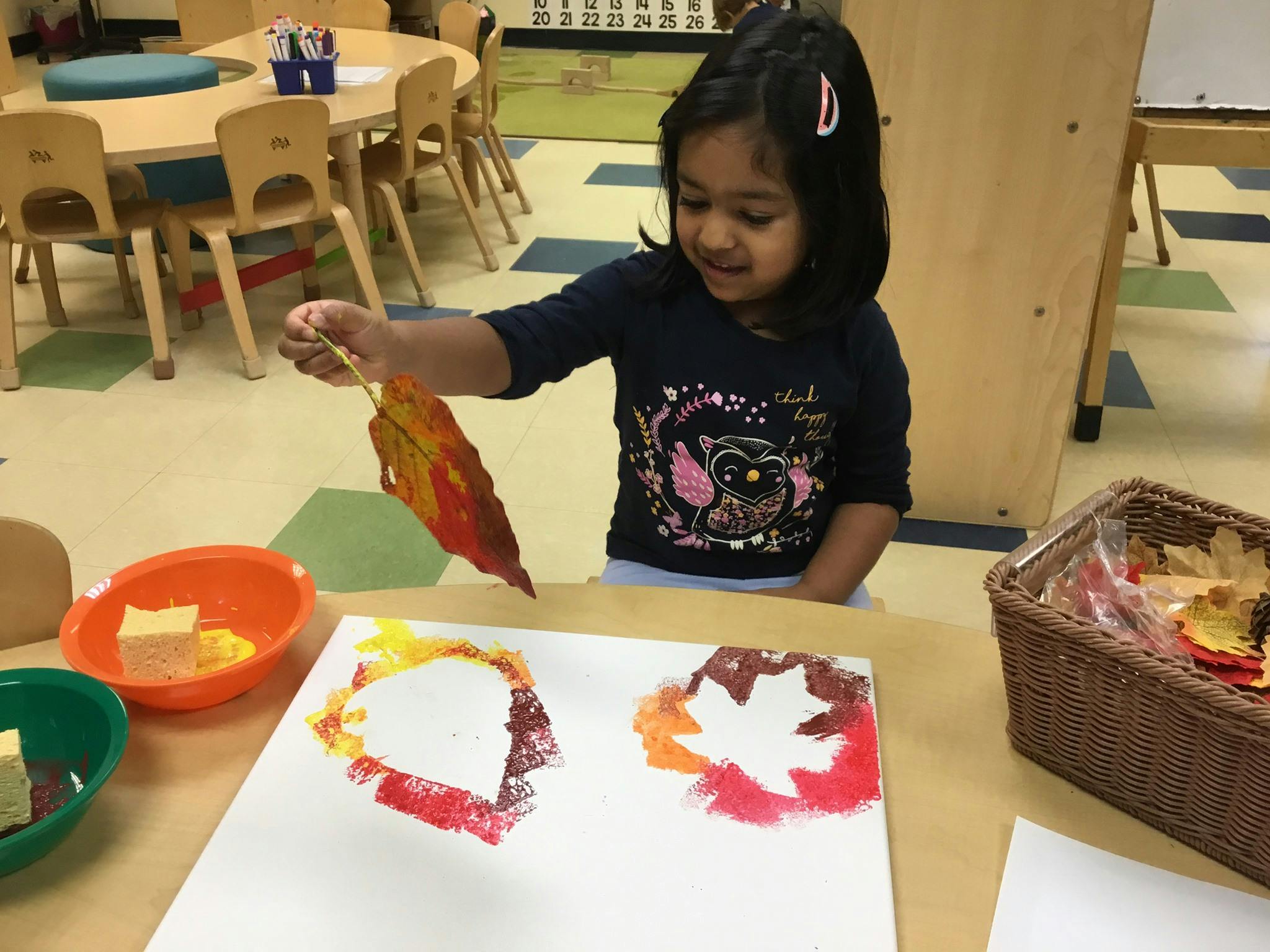 Child holding a leaf over paper with leaf prints in a classroom