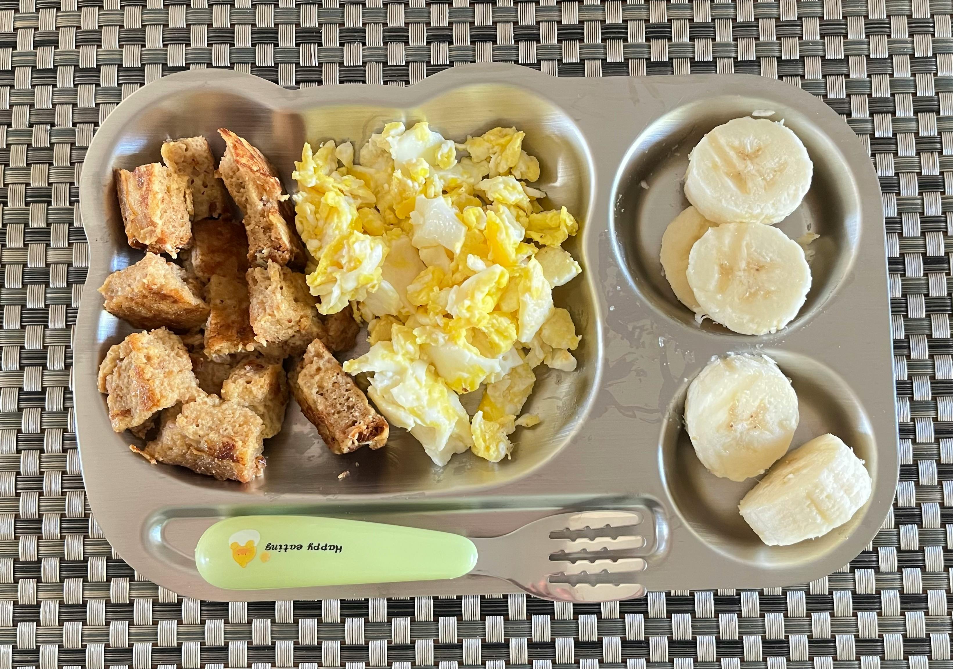 Divided plate with scrambled eggs, bread pieces, and sliced bananas