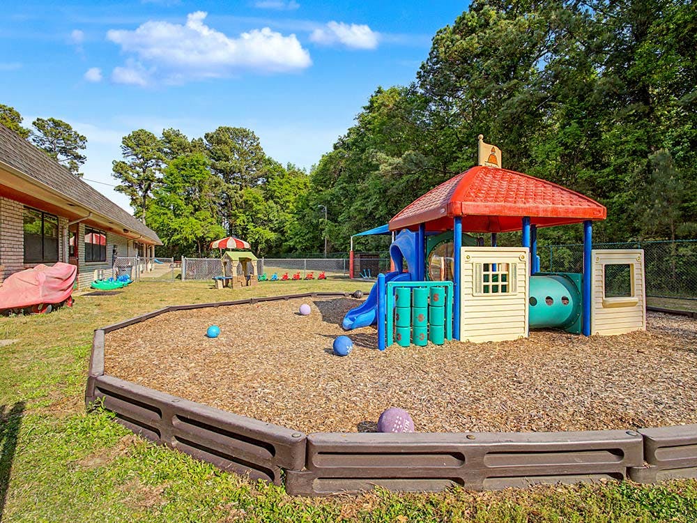 Outdoor playground with a play structure, slide, and tunnel over wood chips