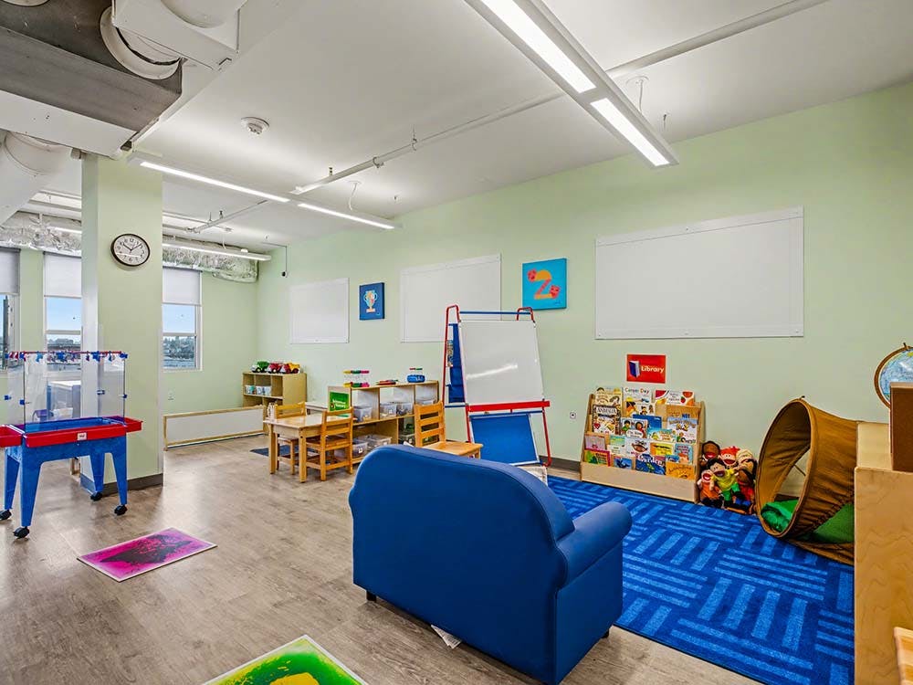 Children's classroom with small tables, chairs, a blue couch, and a bookshelf