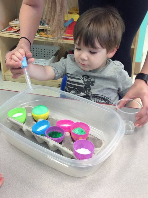 Child using a dropper with colorful cups insets in a plastic container