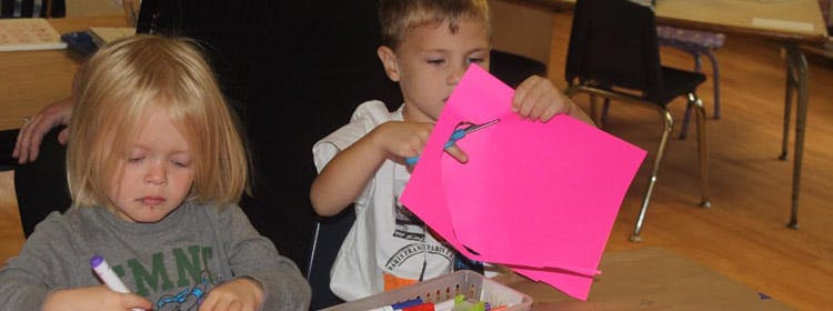 Two children doing crafts, one cutting paper and one drawing