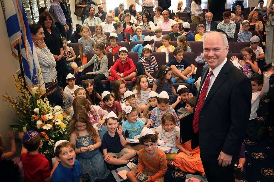 Man in suit standing in front of a group of children and adults