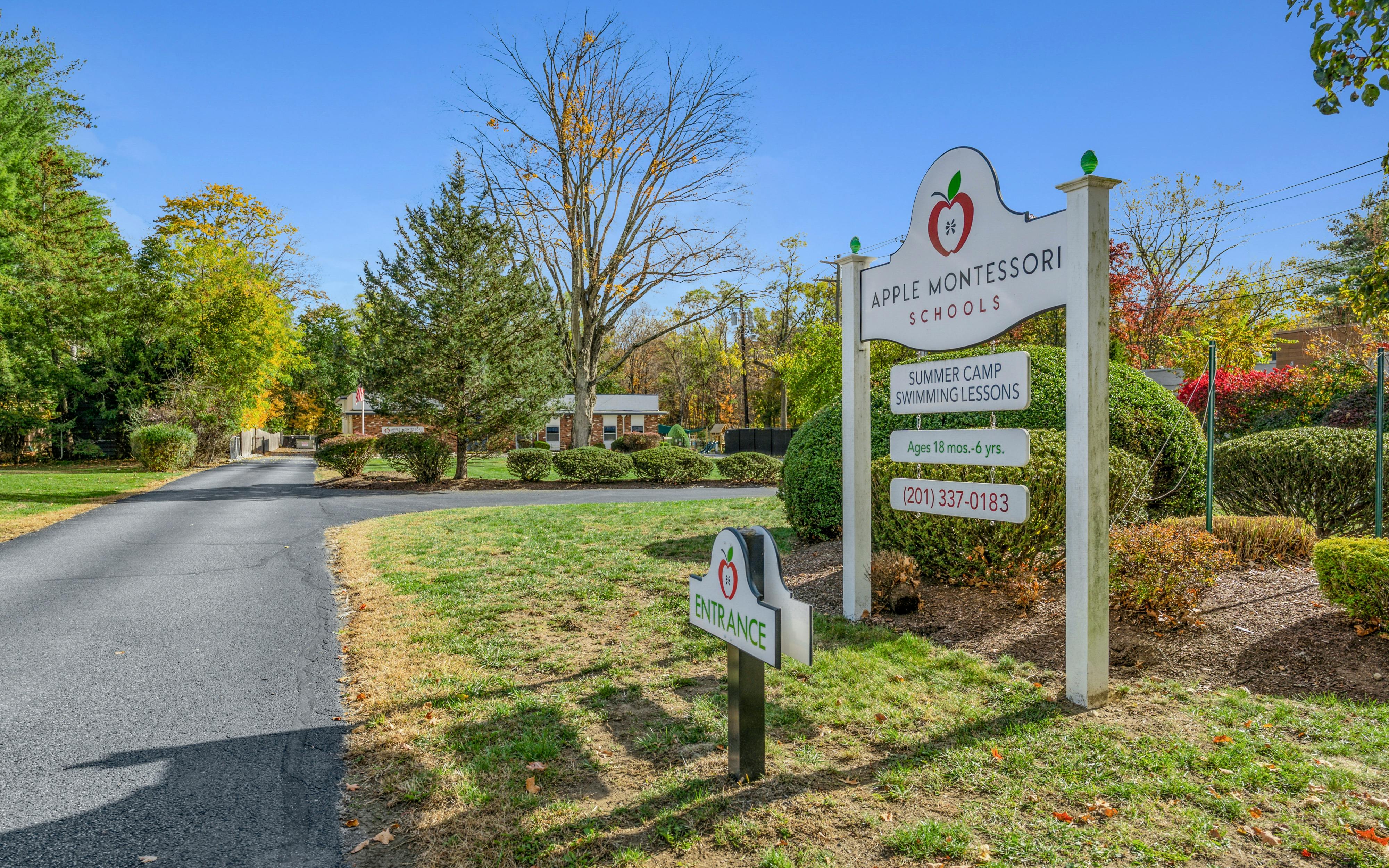 An Apple Montessori Schools sign by a paved driveway leading to a building