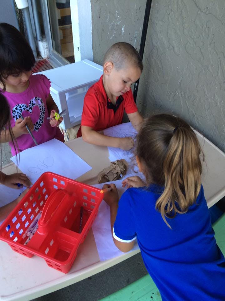 Three children drawing and cutting paper at a table