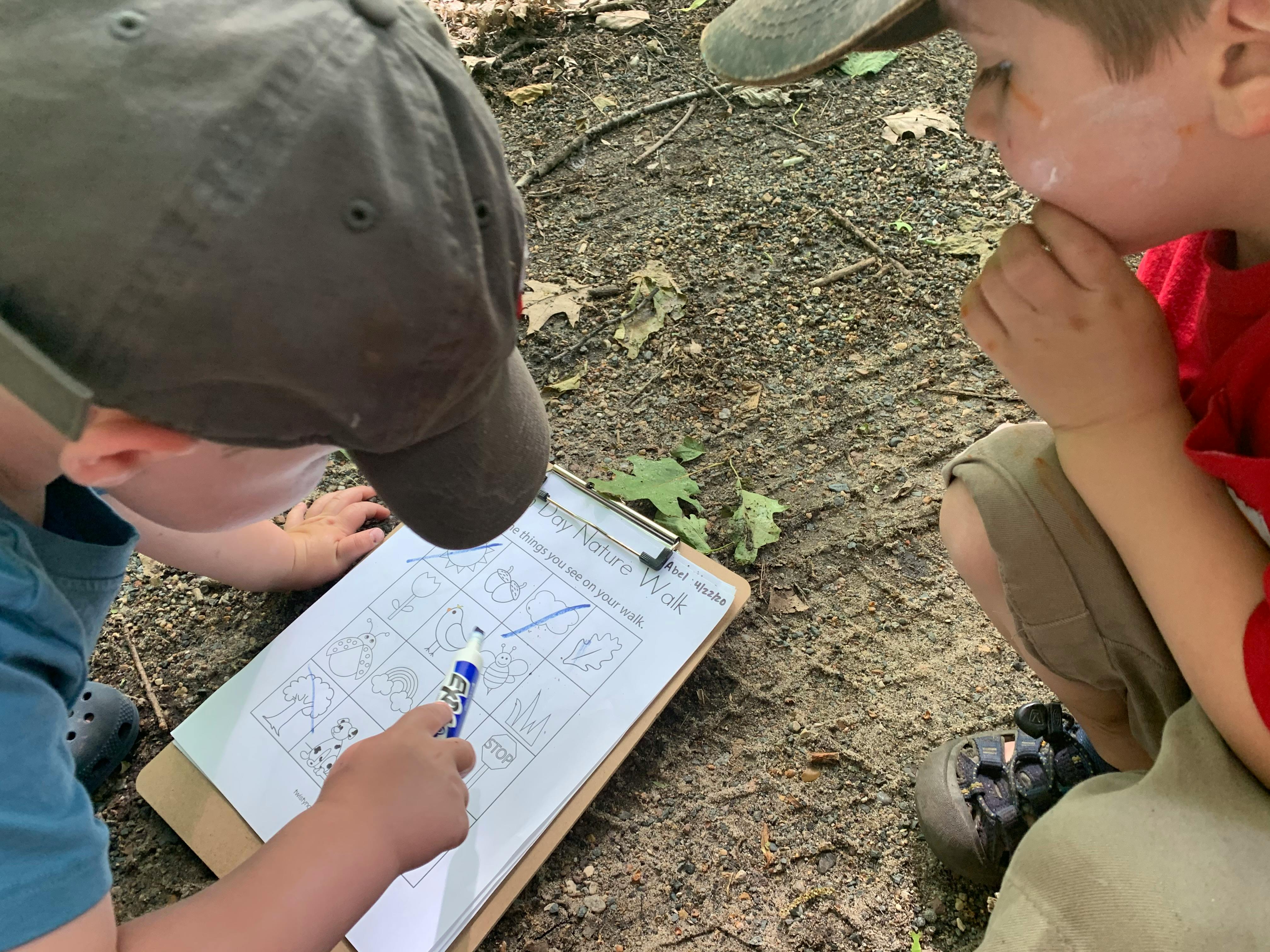 Two children on a nature walk activity, looking at a checklist on a clipboard