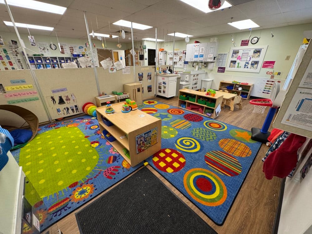 An empty early childhood classroom with colorful rugs and small furniture