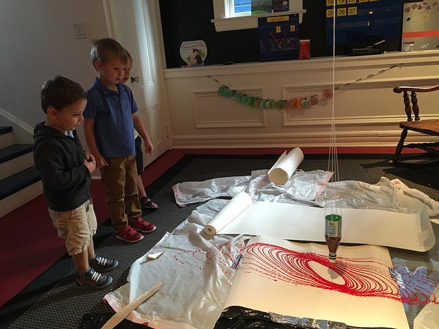 Two children watching a pendulum drawing red lines on paper